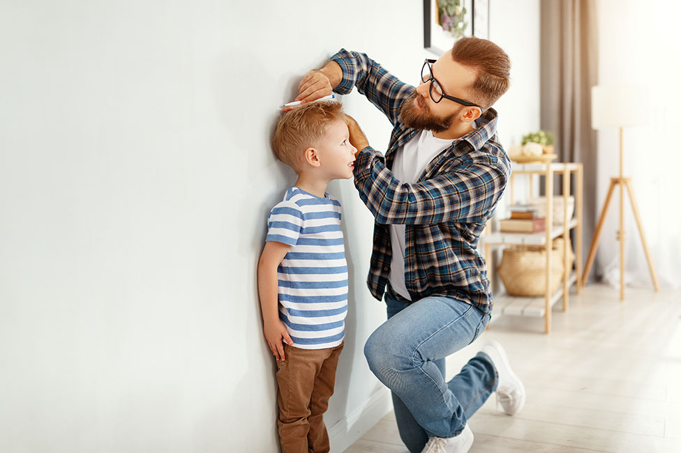 red haired dad marking the height of his young son on the wall of their new house